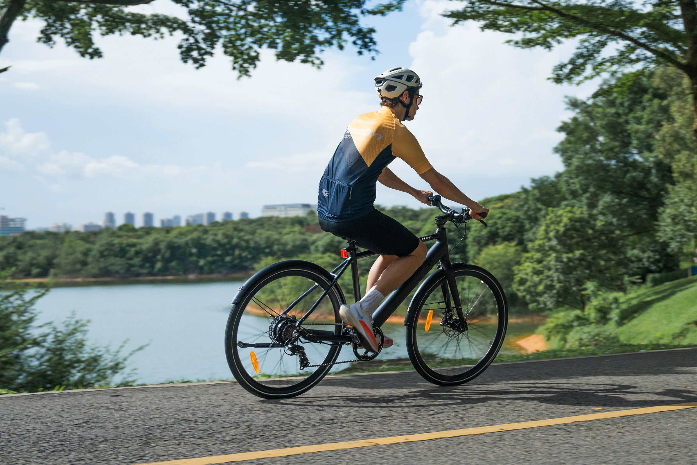 Cyclist wearing a helmet riding a black DYU Stroll 1 electric bike along a lakeside path. Cyclist wearing a helmet riding a black DYU Stroll 1 electric bike along a lakeside path.