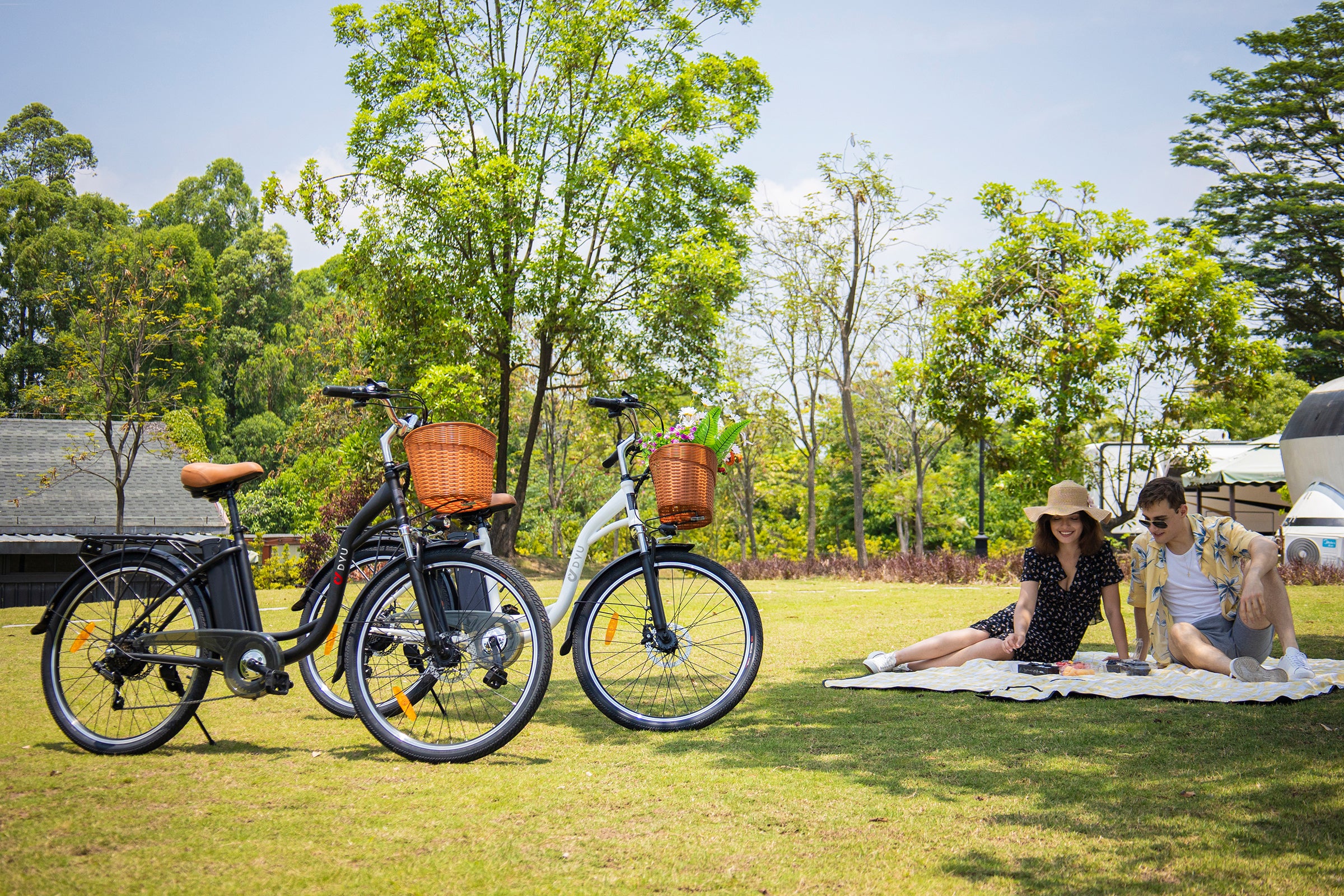 Two people enjoying a picnic near DYU A1F and C6 electric bikes with wicker baskets. Two people enjoying a picnic near DYU A1F and C6 electric bikes with wicker baskets.