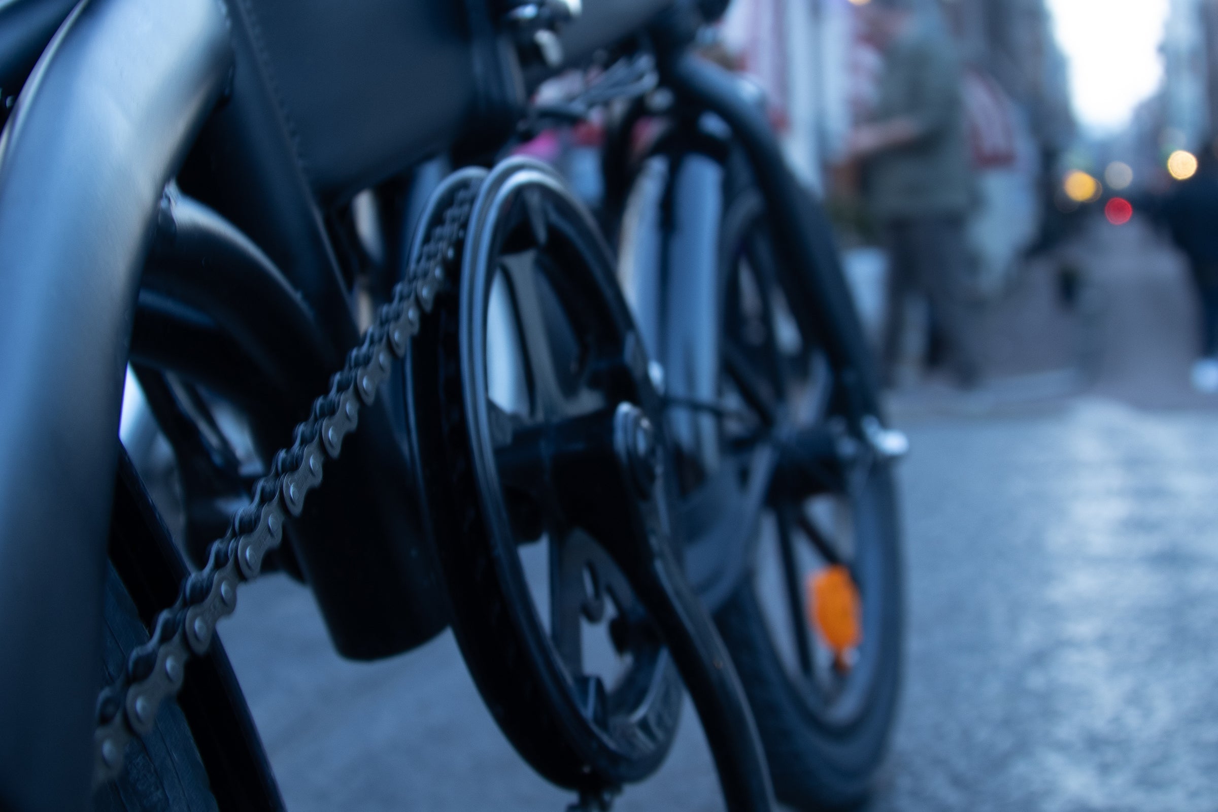 Close-up of the chain and pedals of a DYUcycle electric bike on a city street. Close-up of the chain and pedals of a DYUcycle electric bike on a city street.
