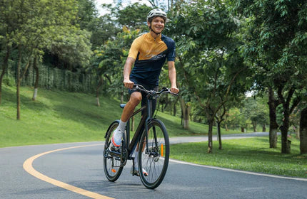 A person is riding a black electric bicycle on a curved path surrounded by greenery and trees.