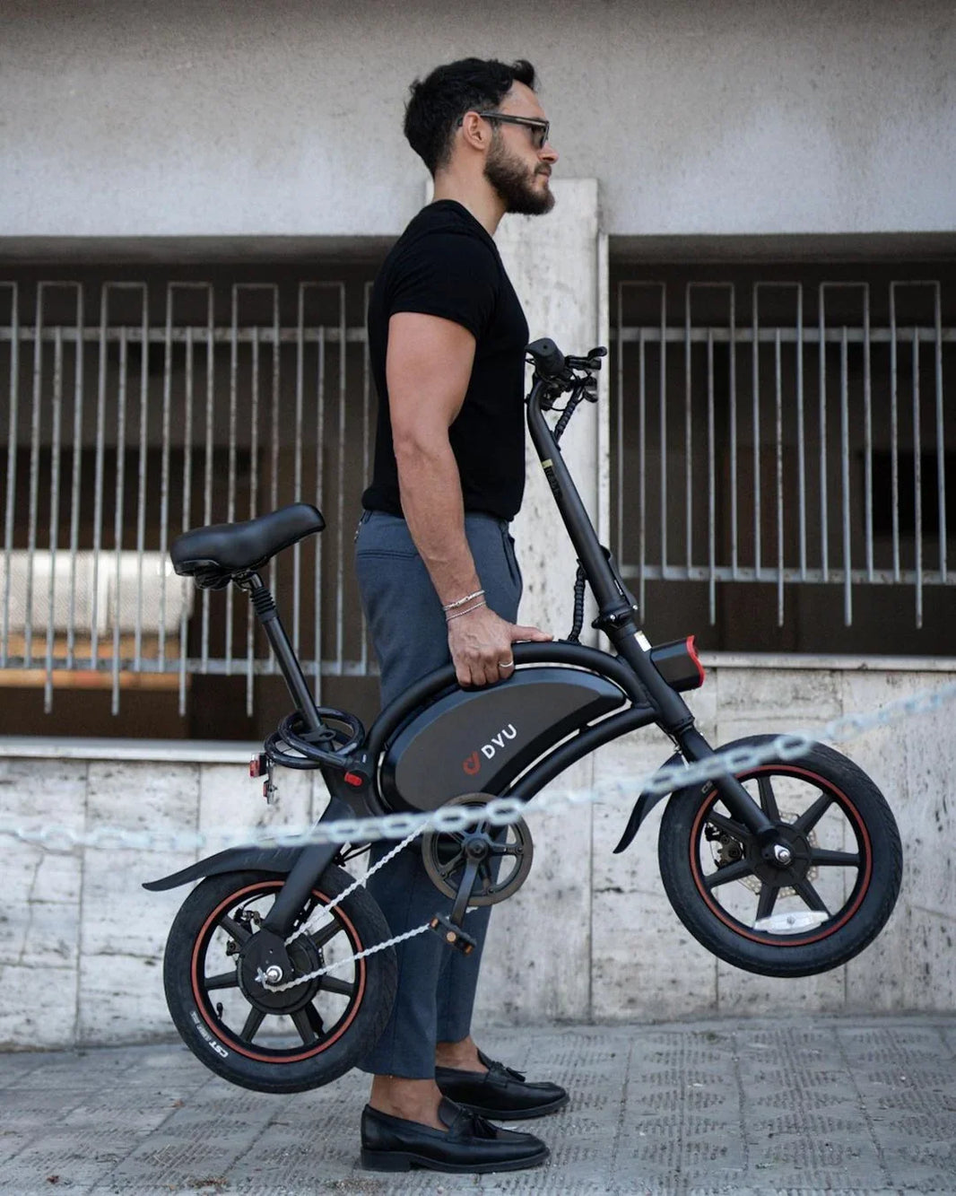 DYU D3F folding e-bike carried by a man beside an urban wall