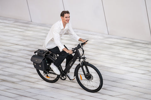 Man riding matte black DYU C5 electric bike with rear rack on modern urban path.