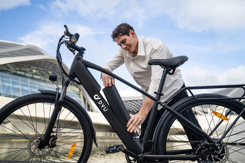 Man detaching removable battery from matte black DYU C5 electric bike outdoors.