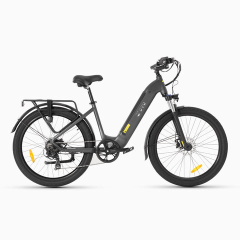 Two grey DYU C1 26 Inch City Electric Bikes on the beach with people relaxing nearby.