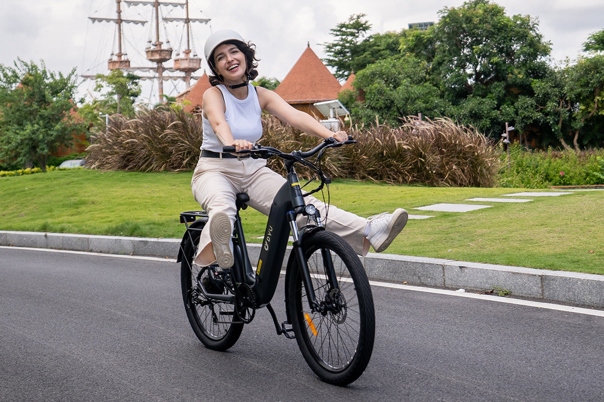 Woman riding grey DYU C1 26 Inch City Electric Bike with front suspension, smiling and stylish.